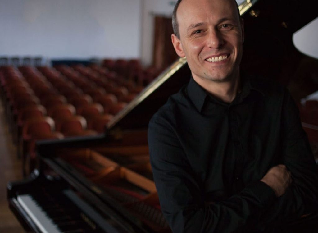 Grzegorz Marszałek, nauczyciel gry na pianinie, stojący przed fortepianem